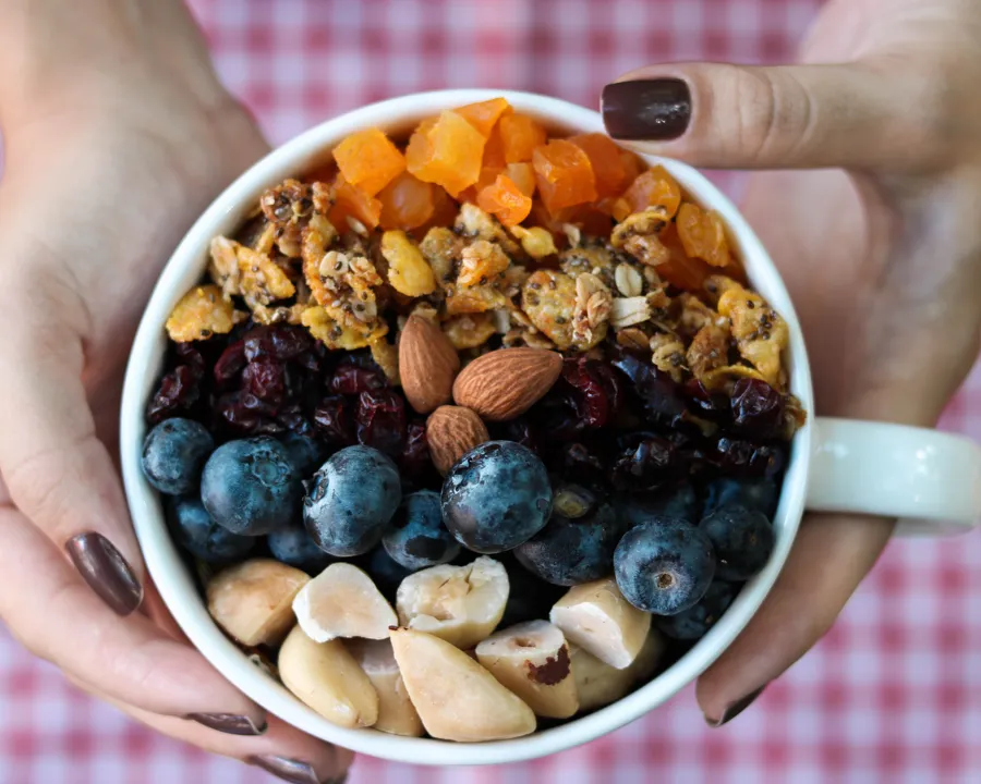 Mãos segurando uma xícara com granola e frutas